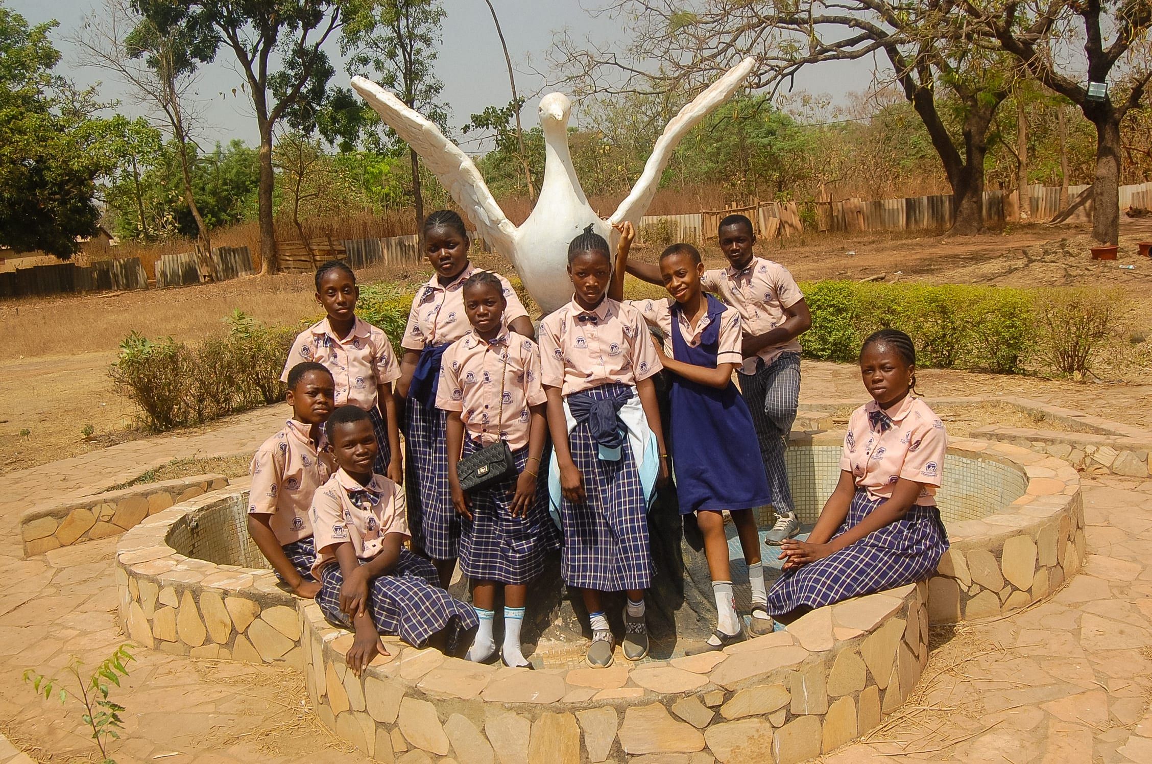 Des élèves rassemblés autour d’une sculpture d’oiseau blanche sur une fontaine en pierre lors d’une sortie éducative.