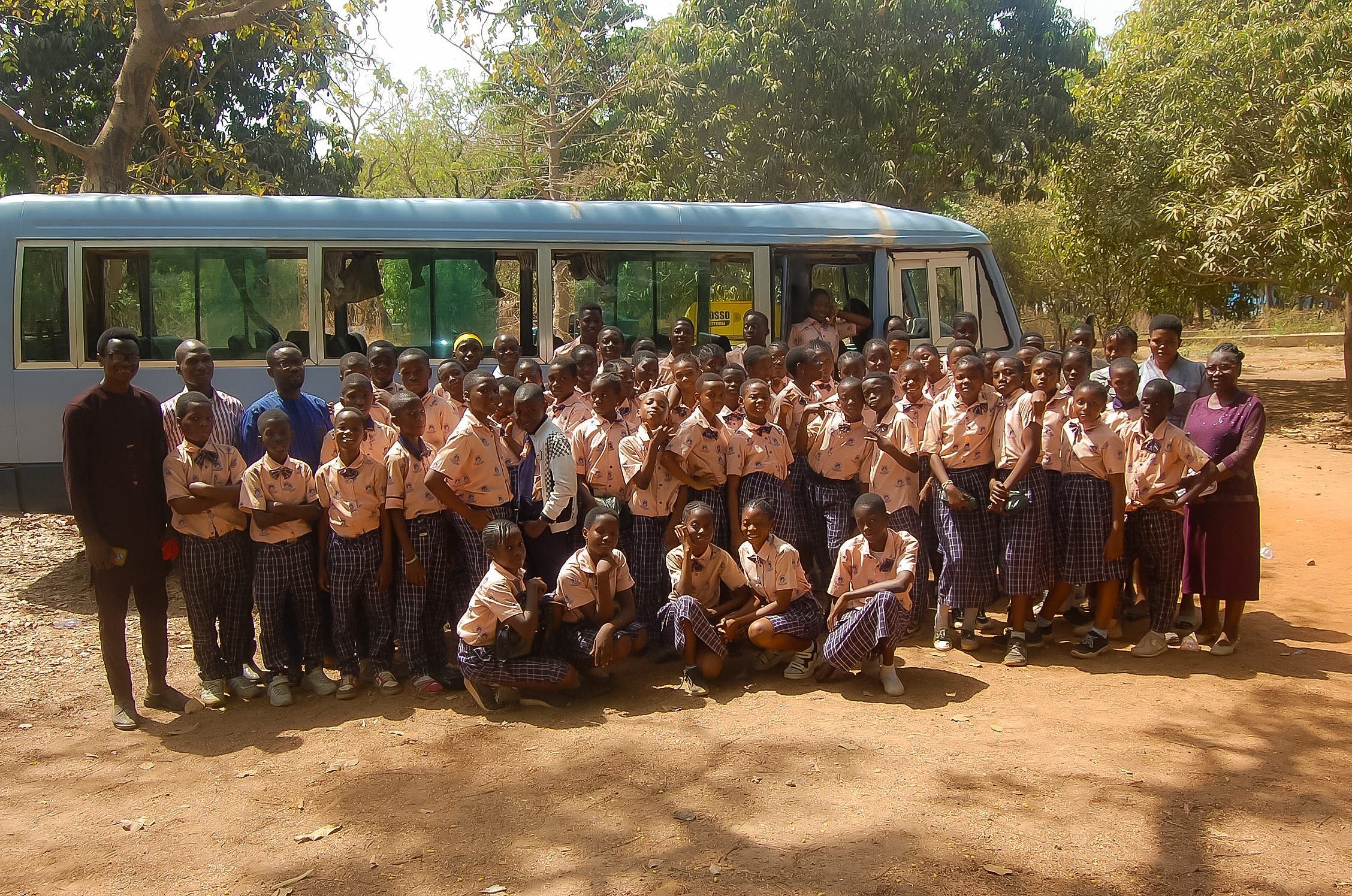 Un grand groupe d’élèves en uniforme, accompagnés d’adultes, réunis devant un car lors d’une sortie éducative.
